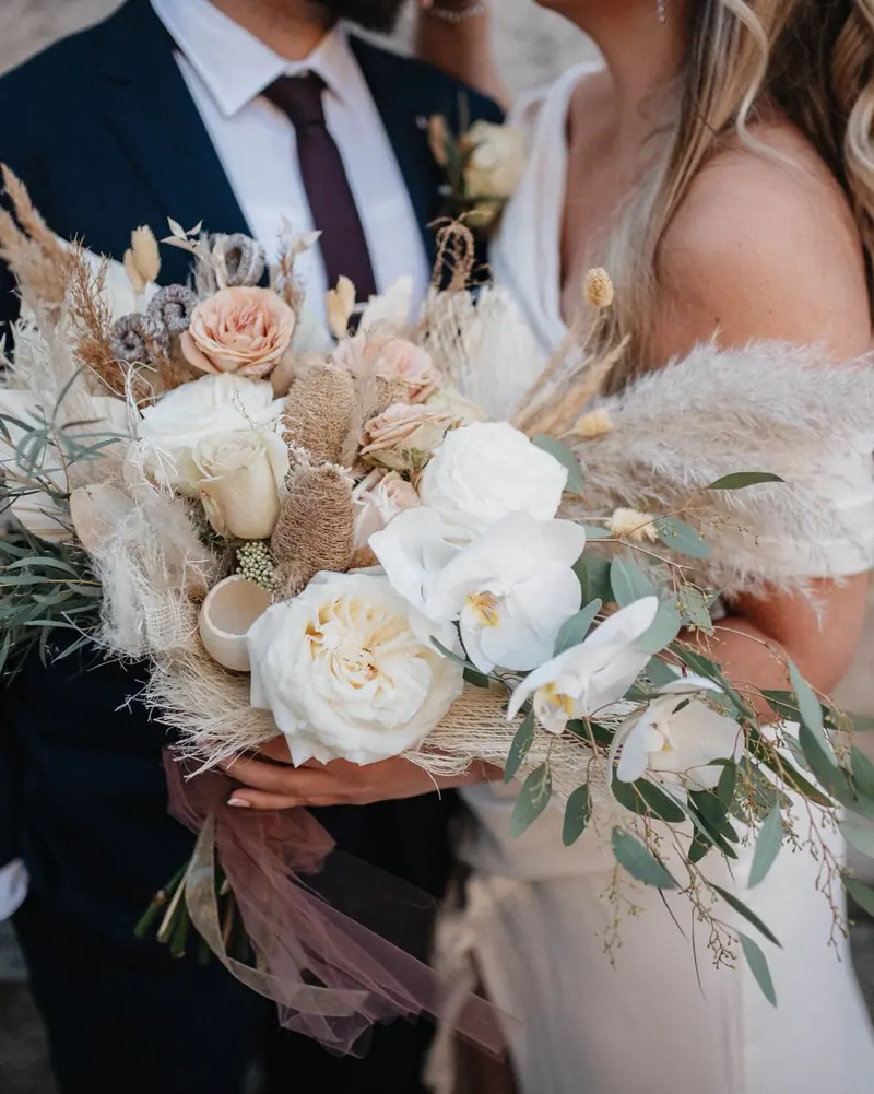 A couple holding a bouquet of roses, orchids and eucalyptus